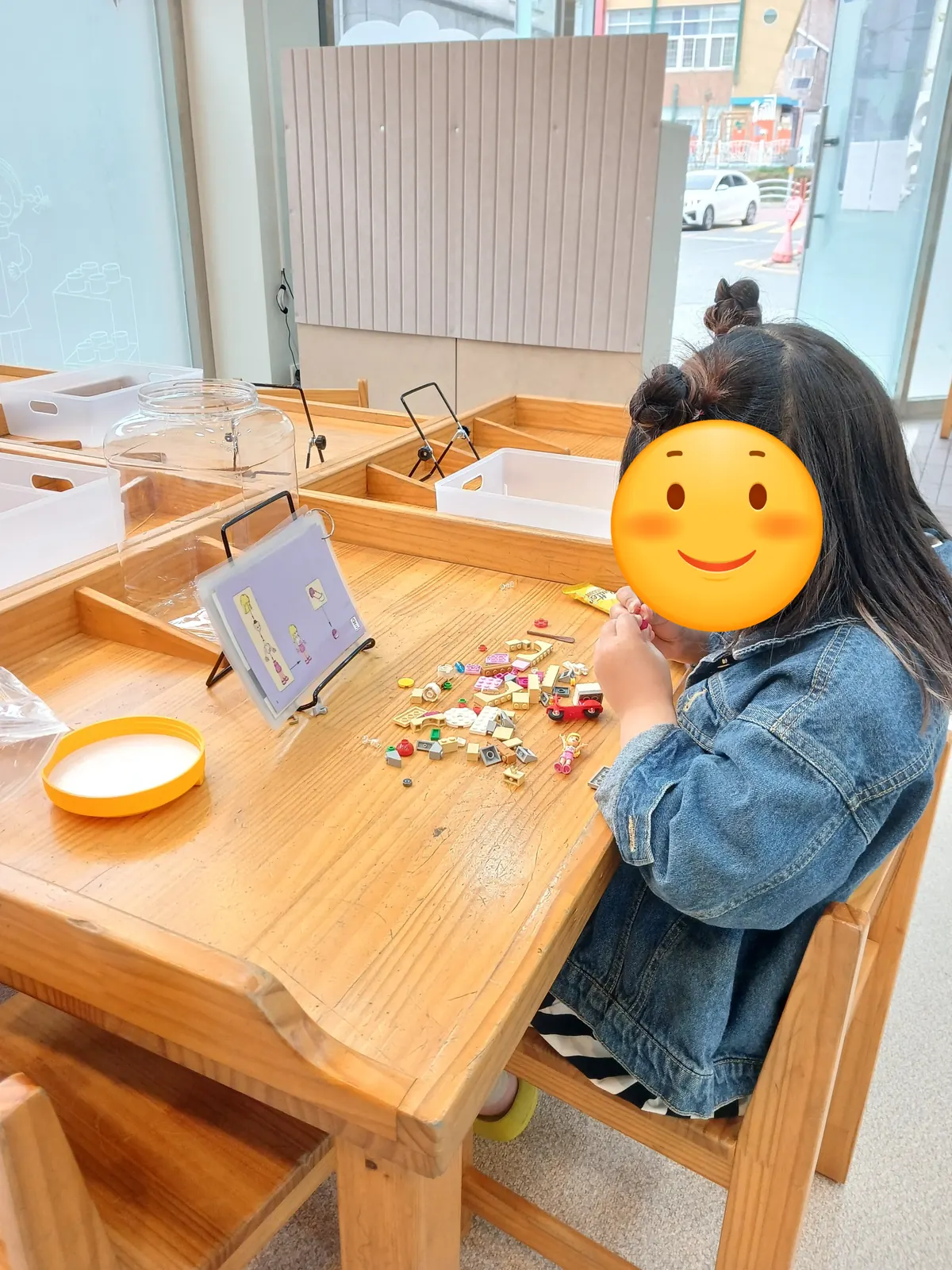 창가 원목 레고 테이블에서 설명서 거치대를 보며 레고를 조립하는 아이