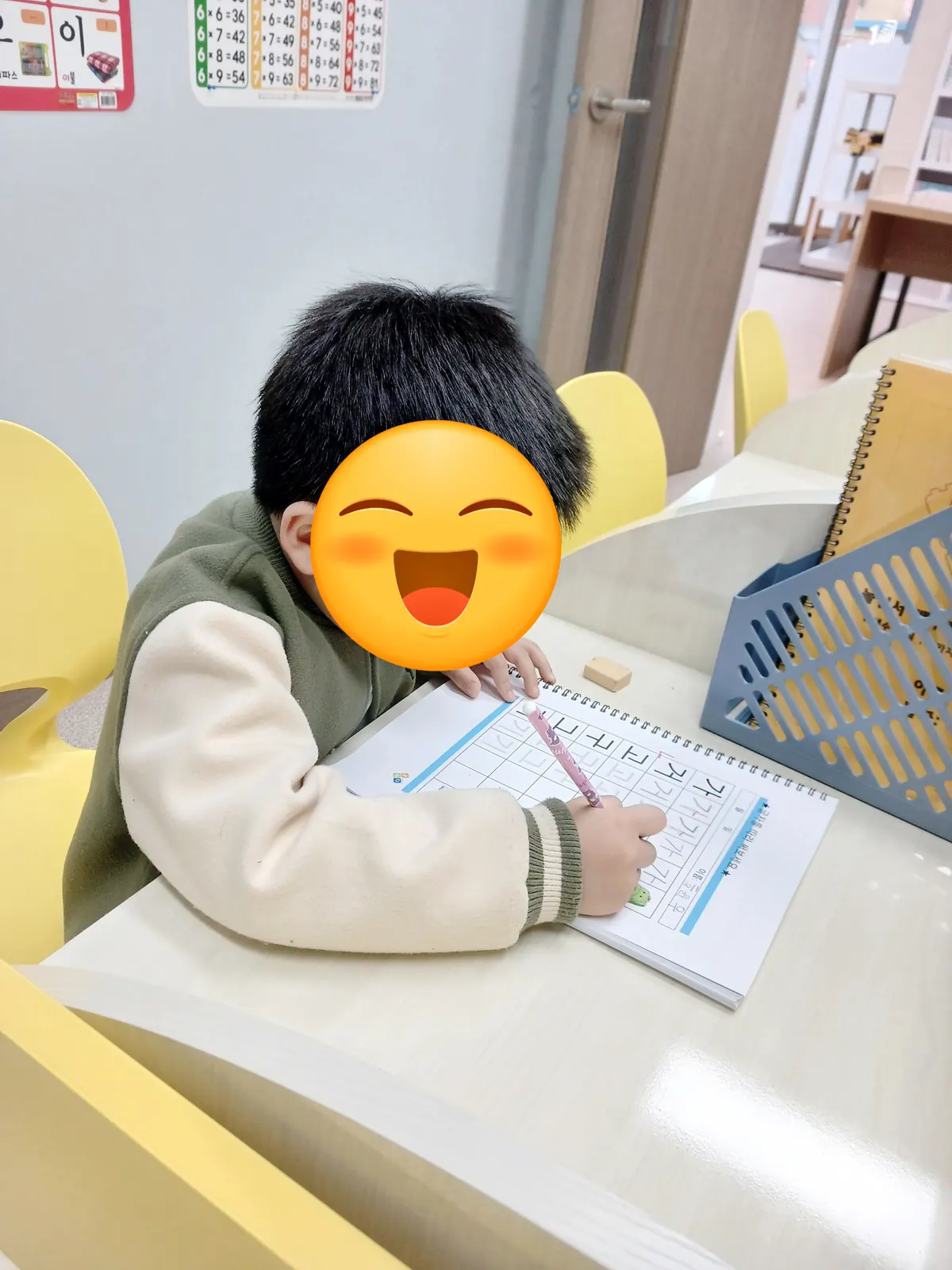 노란 칸막이 책상에서 한글 따라 쓰기 교재에 연필로 쓰는 아이