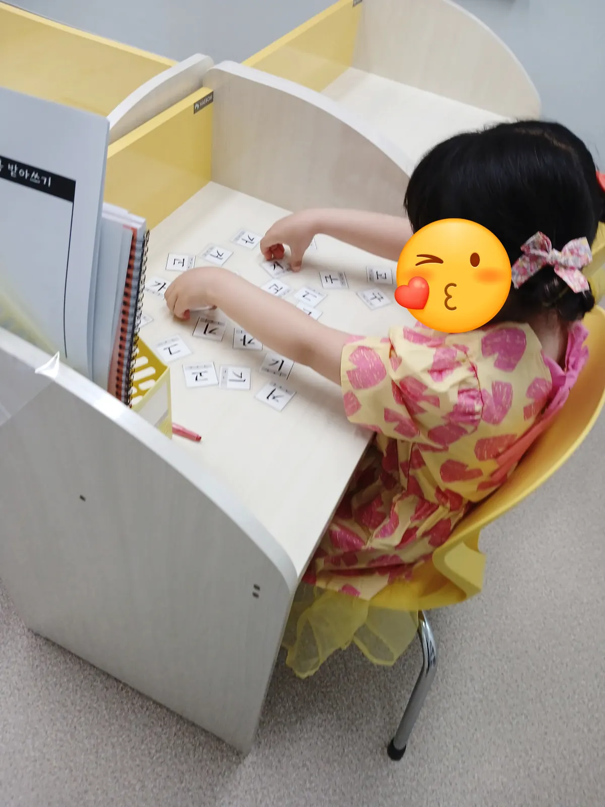 노란 칸막이 책상에서 한글 음절 카드를 맞추는 아이