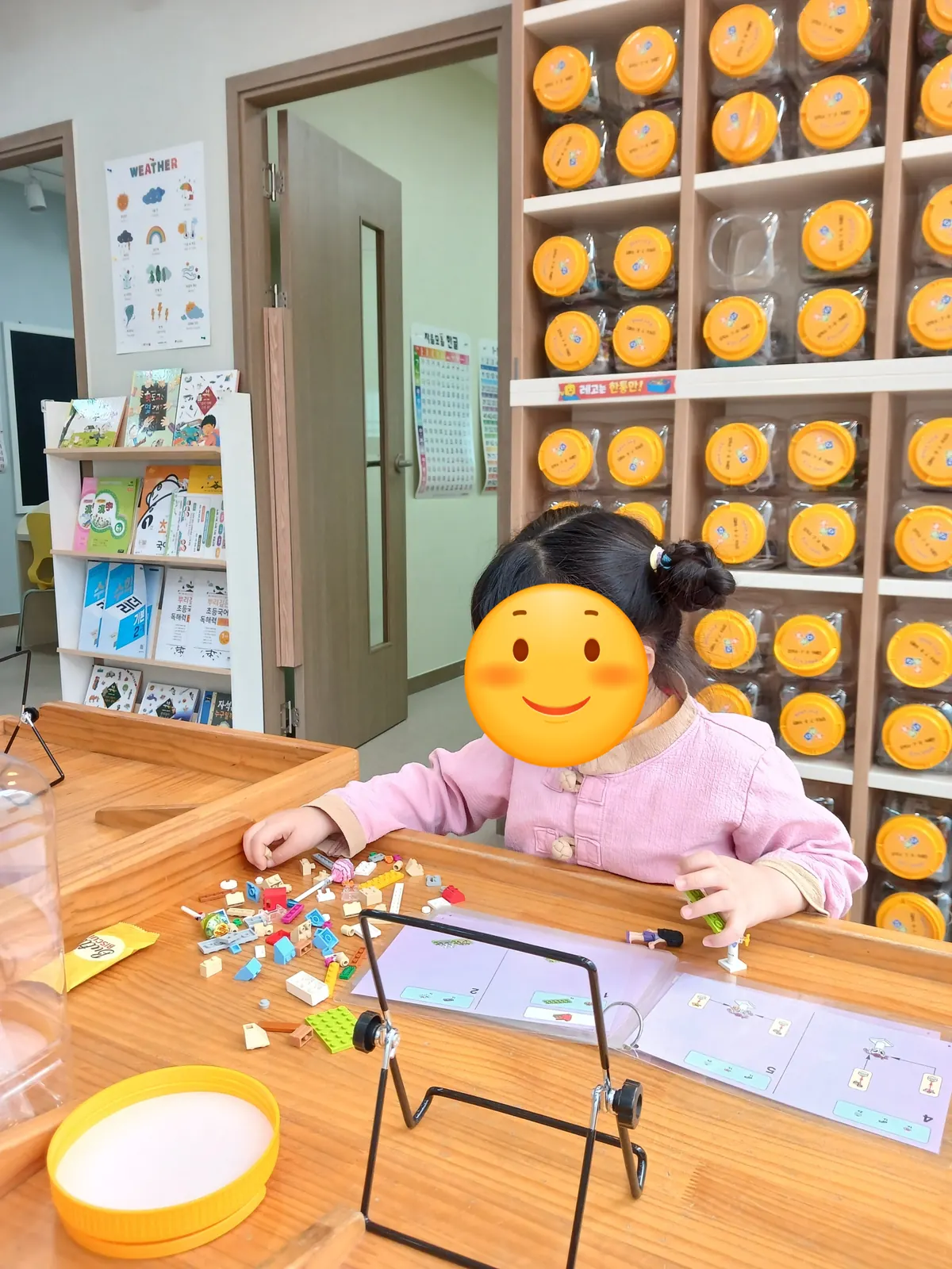 주황 레고 수납장 앞 원목 테이블에서 설명서를 보며 레고를 조립하는 아이