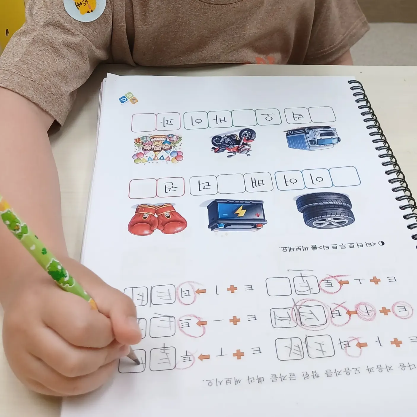트이다 한글 교재에 초록 연필로 받침 글자를 쓰는 아이의 손